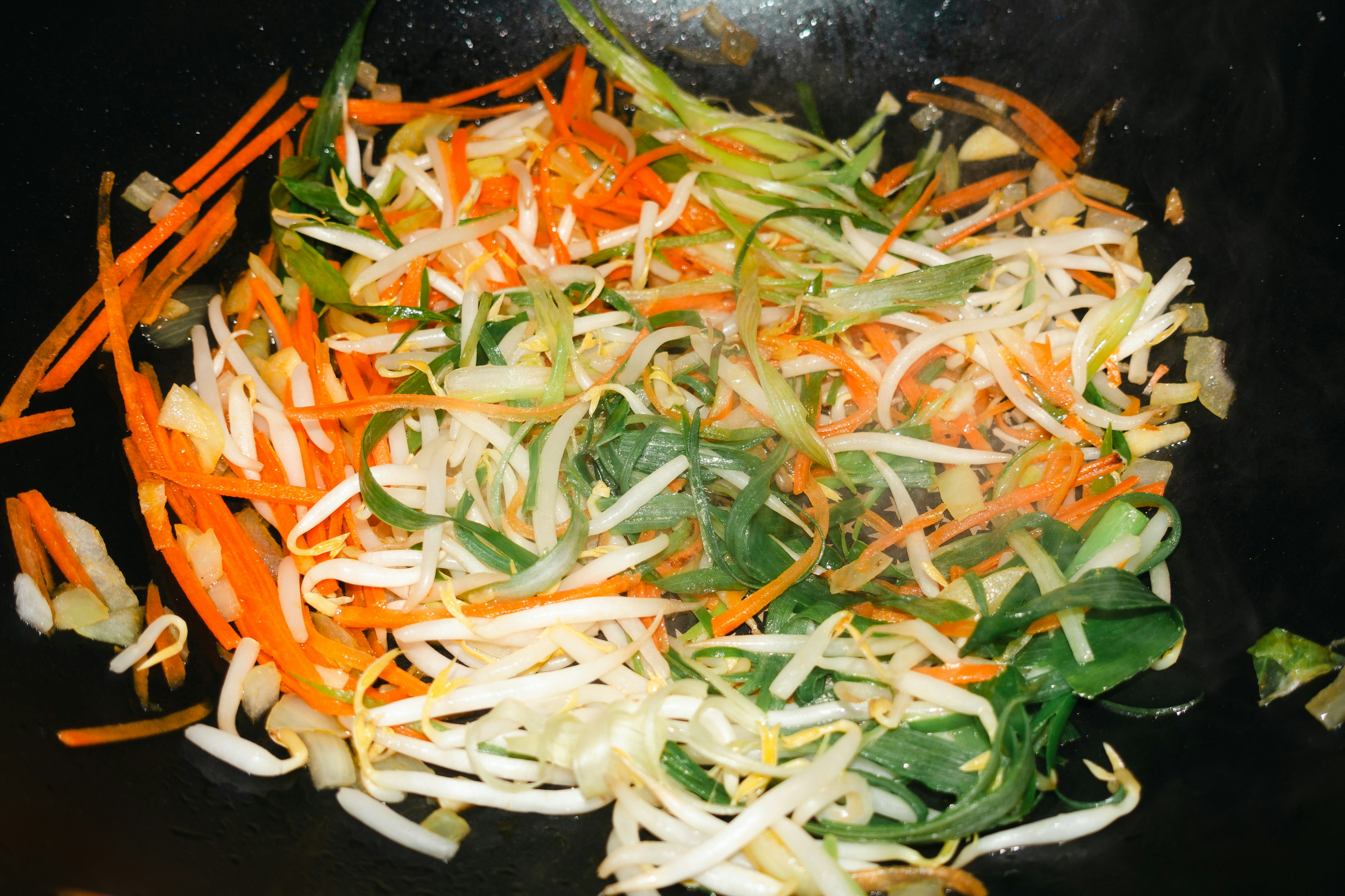 shredded carrots, spinach, and other vegetables in a wok